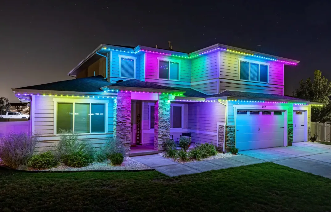 Multicolor outdoor lights outlining the eaves, porch and garage of a two-story home at night